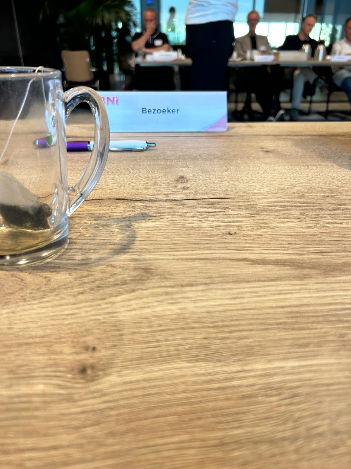 BNI-lidvergadering met gastsprekers aan tafel, inclusief naamplaatje en voorzieningen zoals waterkaraf en penhouders.